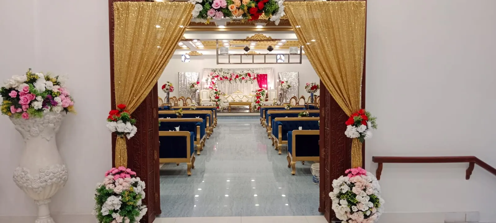 Main hall through gold-draped doors, blue velvet sofas leading to a floral stage